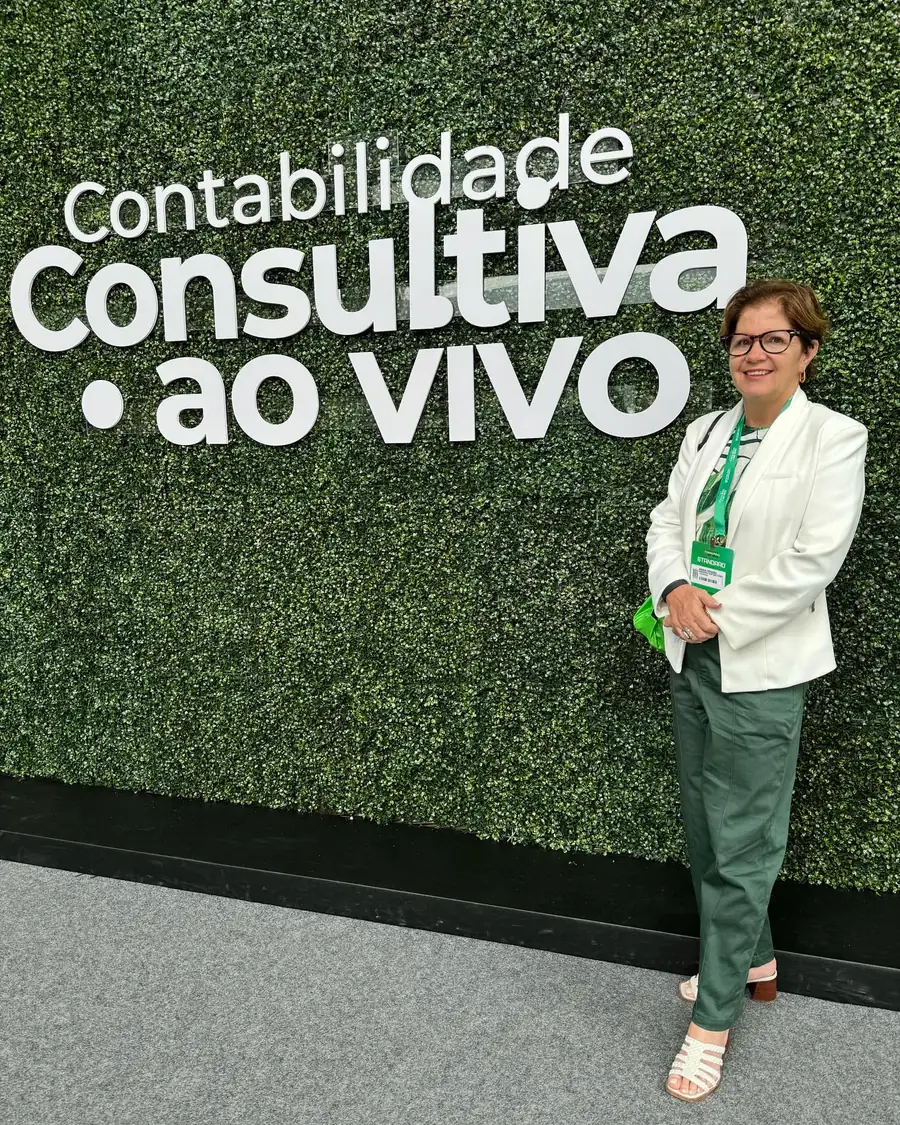 Maria do Carmo Teixeira, de blazer branco, em frente ao painel verde do evento Contabilidade Consultiva ao Vivo